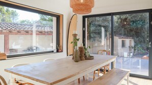 A dining area with a long wooden table, wicker chairs, and a large window offering a view of the outside. - Beautiful home in Pernes-les-Fontaines (Pernes-les-Fontaines)
