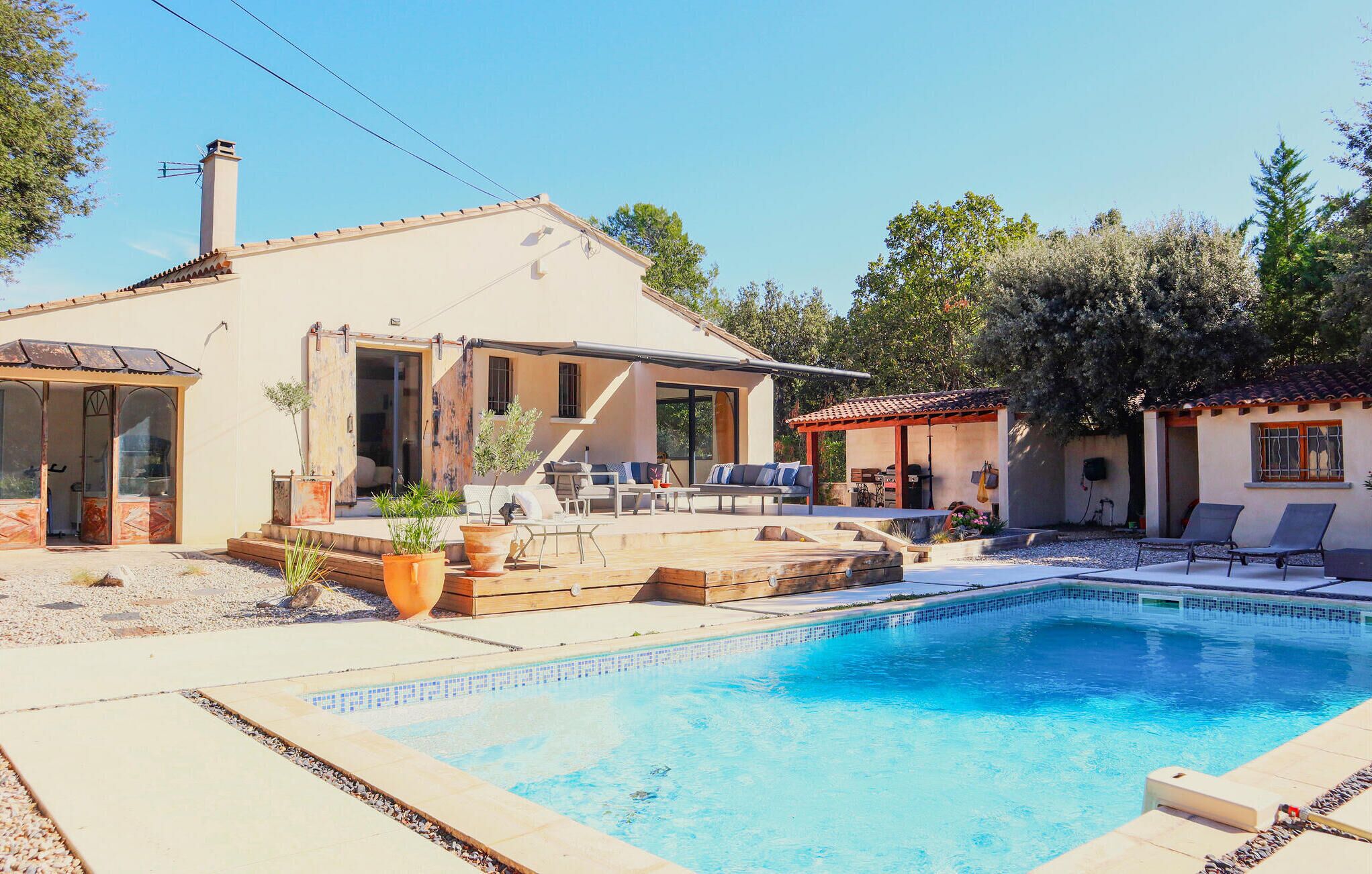 Une maison avec une piscine, du mobilier de jardin et un espace extérieur aménagé avec un coin salon couvert.