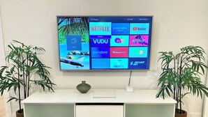 A flat-screen TV mounted on a wall displaying a home screen with various streaming apps. - 3Bd, 1 bath - Centrally located 15min Airport/Bellevue/Seattle/TopGolf/Hiking (Renton)