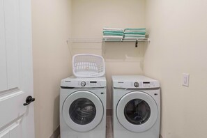 A laundry area with two Samsung washing machines, a white basket, and a shelf with folded towels. - 2971 Castaway Lane (Kissimmee)