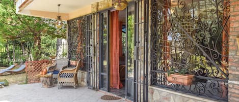 A covered outdoor area with wicker furniture, a stone wall, and metal gates.