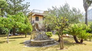 A garden with a stone fountain, various trees, and a building with a balcony in the background.