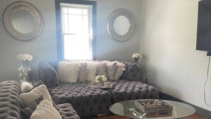 A modern living room with a sectional sofa, a glass coffee table, and decorative vases. - The River Green Getaway
 (Fort Wayne)