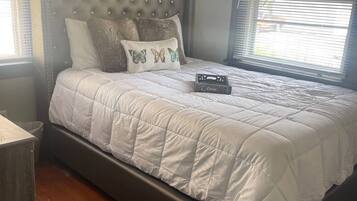 Un dormitorio con cabecera capitonada, edredón blanco acolchado y cojines decorativos.