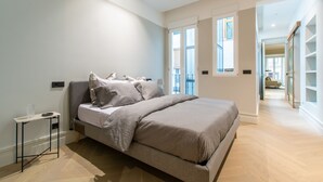 A modern bedroom with a large bed, a bedside table, and a view of the outside through a window.