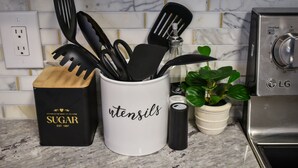 Una encimera de cocina con utensilios, un recipiente de azúcar, una planta en maceta y un microondas LG.