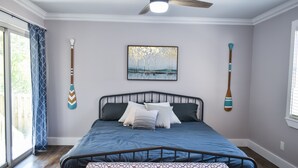 Un dormitorio con cama, ventilador de techo, ventana y un cuadro en la pared.