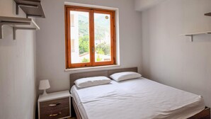 Ein Schlafzimmer mit Bett, Nachttisch, Fenster mit Blick auf Grünflächen und einem Holzkopfteil.