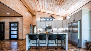 A modern kitchen with a central island, stainless steel appliances, and a wooden floor.
