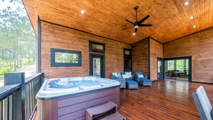 A wooden deck with a hot tub, outdoor seating, and a view of the forest.