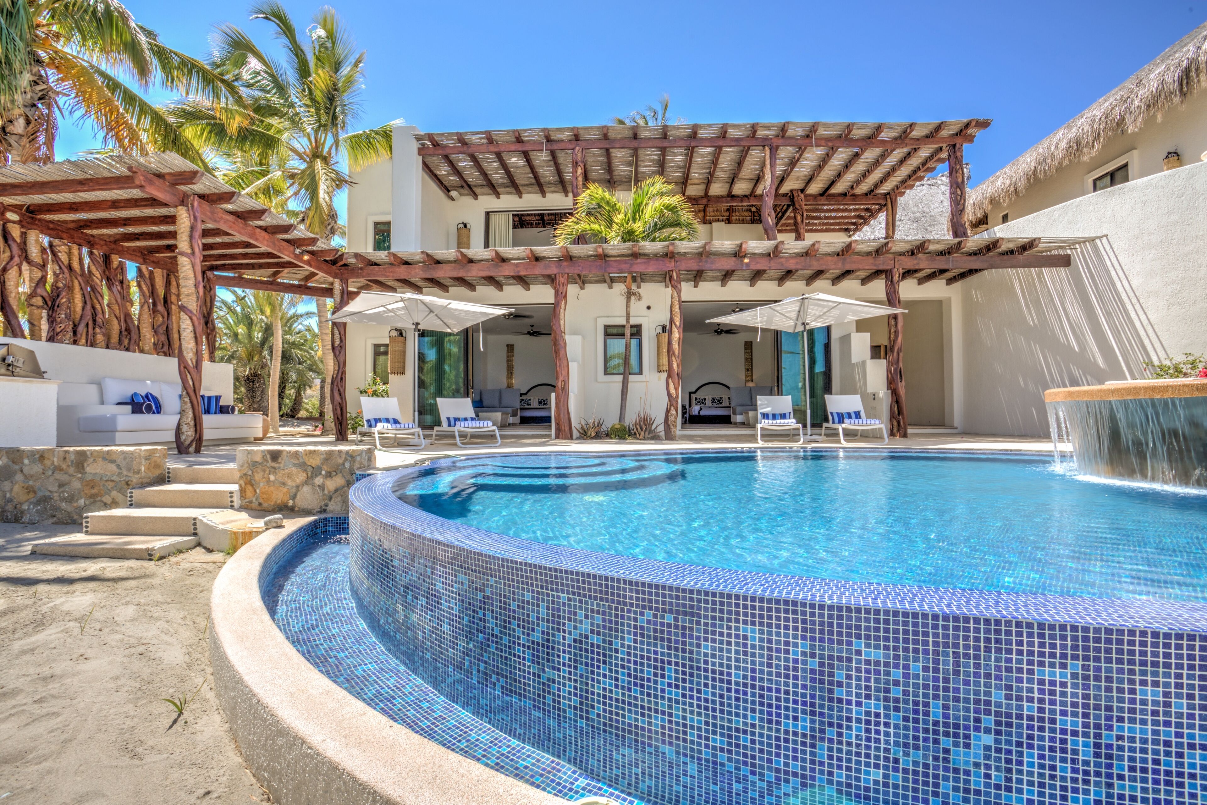 A swimming pool with a tiled edge, lounge chairs, and a covered seating area with umbrellas.