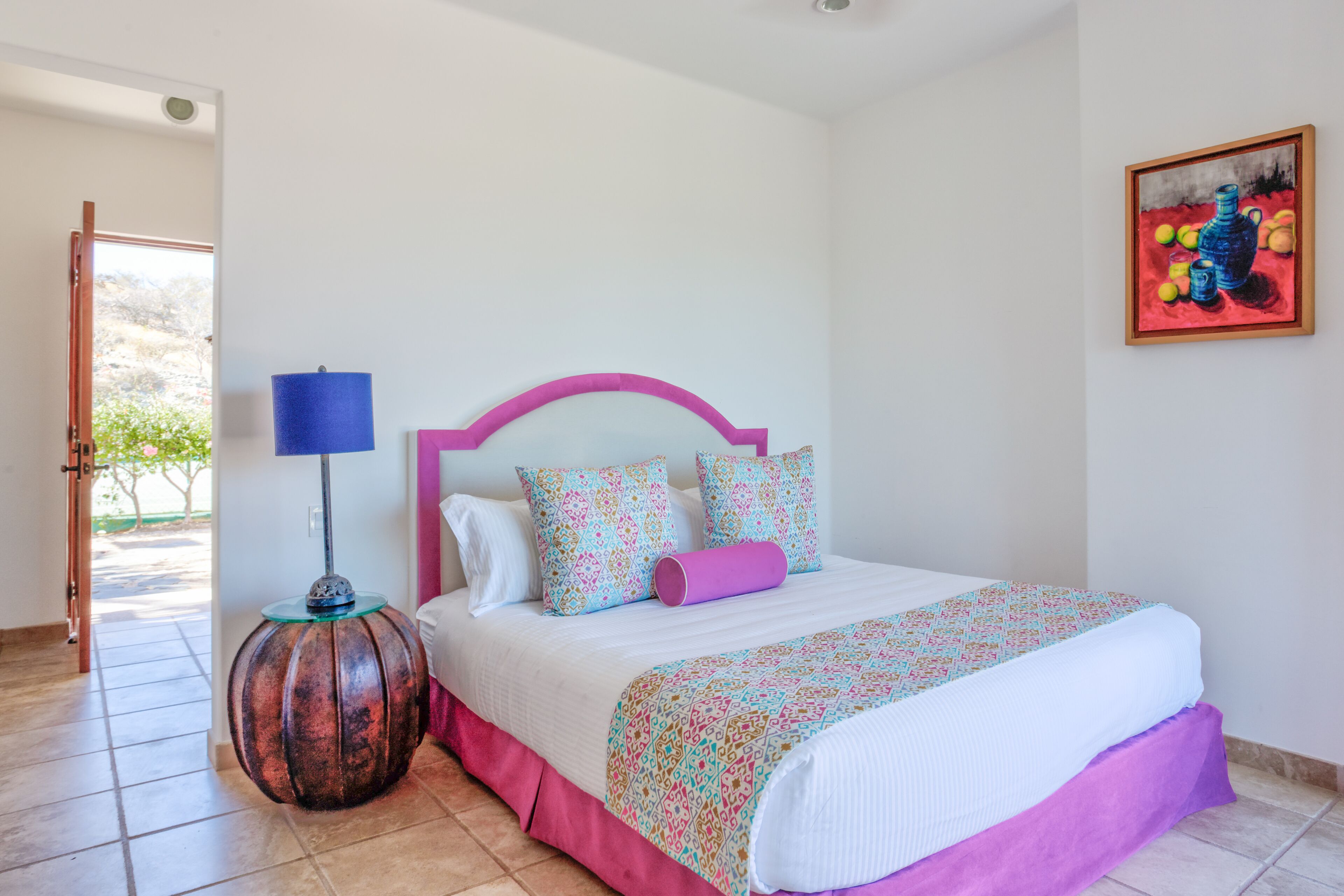 A bedroom with a bed, a lamp, and a painting on the wall.