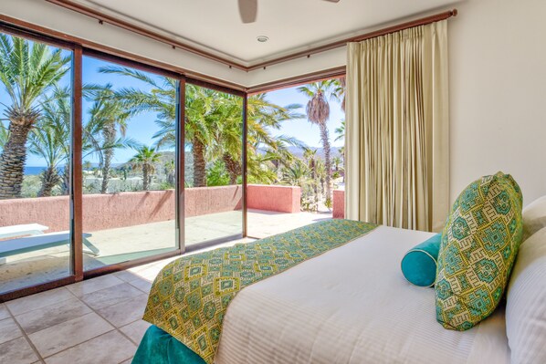 Un dormitorio con una cama grande, vistas a palmeras y un balcón.