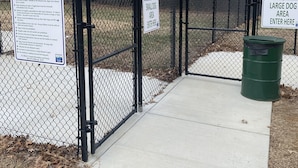 A fenced dog park area with signs indicating separate sections for small and large dogs.
