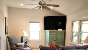 A living room with a ceiling fan, a television, a blue sofa, a wicker chair, and a glass coffee table.