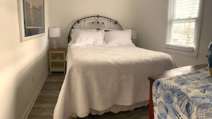 A neatly arranged bedroom with a bed, bedside lamps, a small nightstand, and a window with blinds.