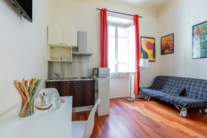 A compact room with a kitchenette, a sofa, a dining table, and a window with curtains.