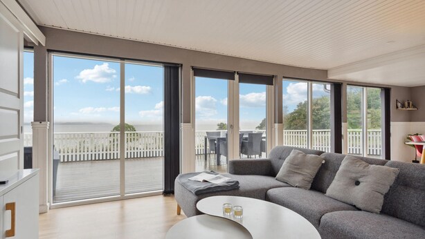 A modern living room with a grey sofa, a white coffee table, and large sliding glass doors leading to a balcony with a white fence and a view of the sea. - Amazing home in Børkop with WiFi (Børkop)
