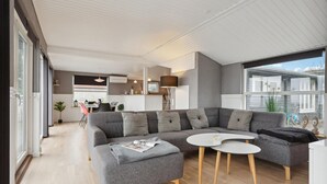 A modern living room with a grey sectional sofa, a small round table, and a kitchen in the background. - Amazing home in Børkop with WiFi (Børkop)