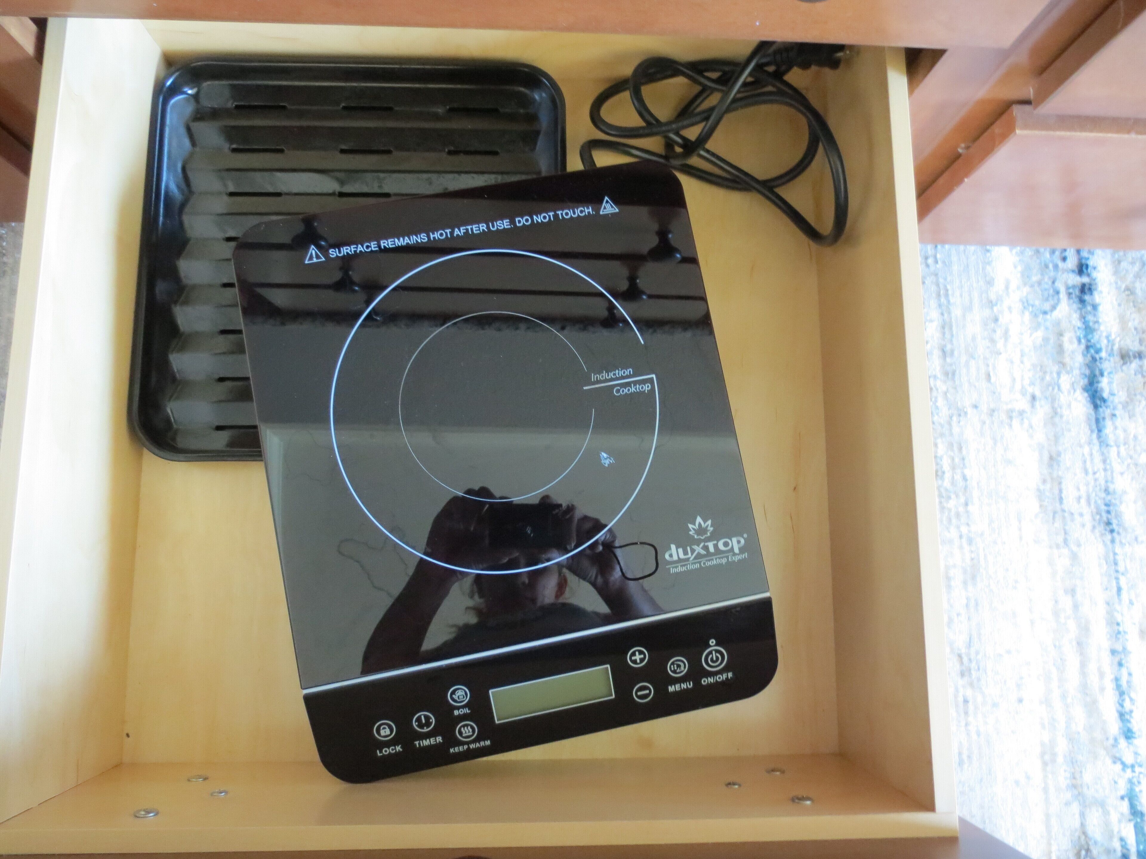 A black induction cooktop with a digital display and control buttons, placed inside a wooden drawer.