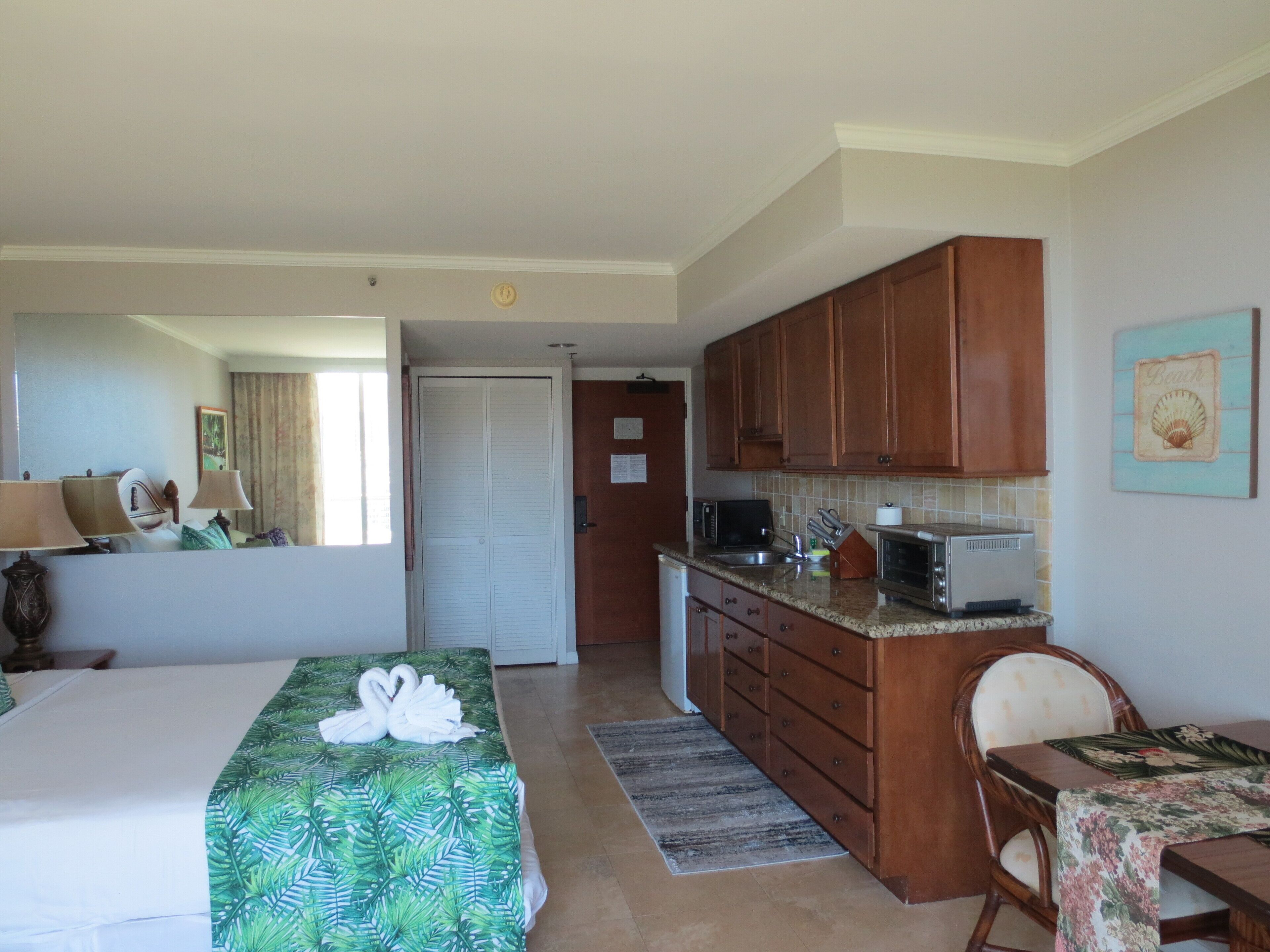 A hotel room with a bed, a desk, a kitchenette, and a bathroom.