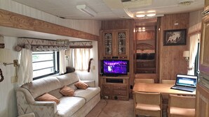 Un intérieur de camping-car chaleureux et confortable, avec un canapé, une table à manger et des chaises, un téléviseur et des meubles en bois.