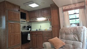 Une cuisine compacte pour camping-car, dotée de meubles en bois, d’une cuisinière, d’un four à micro-ondes et d’une machine à café.