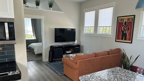 A modern living room with a flat-screen TV, a sofa, a kitchen area with a stove, and a dining table.
