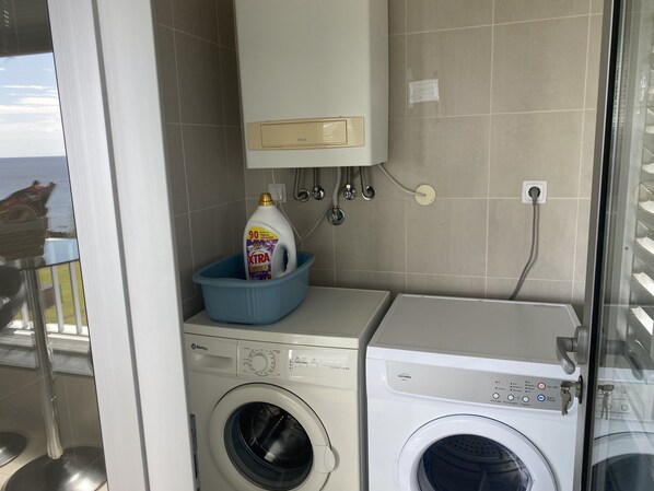 Un área de lavandería compacta con lavadora y secadora, un lavabo azul con detergente y un panel de control instalado en la pared.
