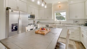 A modern kitchen with white cabinetry, a wooden dining table, and a fruit bowl. - Waterfront Pass Christian Paradise: 1 Mi to Beach (Pass Christian)