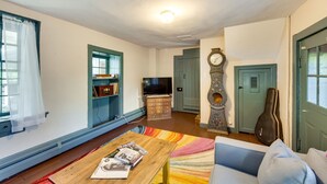 Uma sala de estar com mesa de centro de madeira, sofá azul, televisão, relógio e uma guitarra.