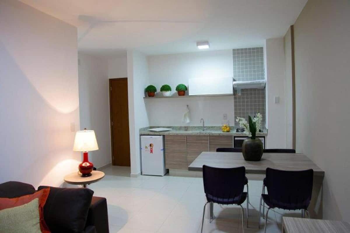 Un espace de vie compact comprenant un coin cuisine, un coin repas avec deux chaises, une petite table et une lampe de sol rouge.