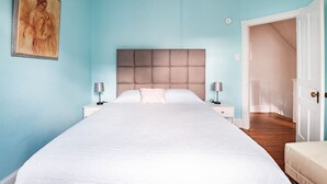 Una camera da letto con un letto grande, due comodini con lampade, una testiera e una porta che dà su un'altra stanza.