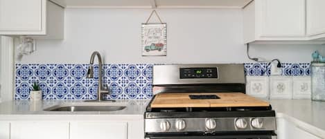 A kitchen with white cabinets, a stainless steel stove, a microwave, and blue patterned backsplash tiles.