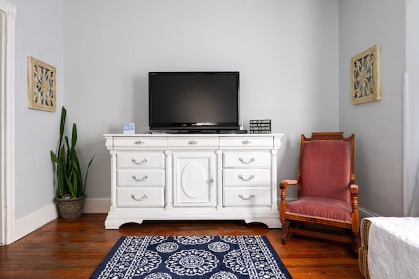 Una habitación con un aparador blanco, un televisor encima, una silla roja y una alfombra estampada.