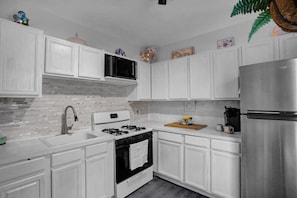 Una cocina moderna con armarios blancos, un refrigerador de acero inoxidable, una estufa a gas y un microondas.