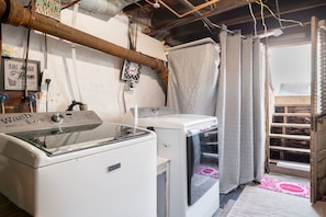 Un área de lavandería con lavadora y secadora, calentador de agua y una ventana con cortinas.