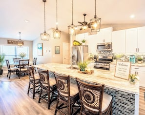 A modern kitchen with a central island, stainless steel appliances, and a dining area with wicker chairs. - Private Resort Retreat • Heated Pool, Spa & Tiki Bar • Pets ok• Beaches nearby  (Vero Beach)