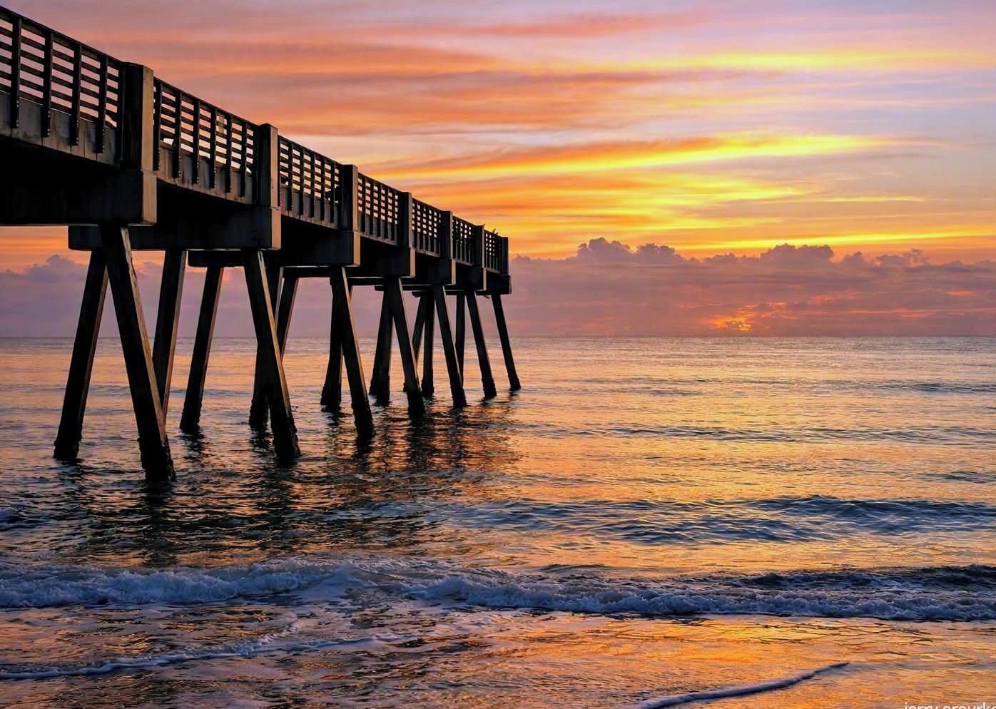 Un muelle que se adentra en el agua, con un atardecer de fondo.