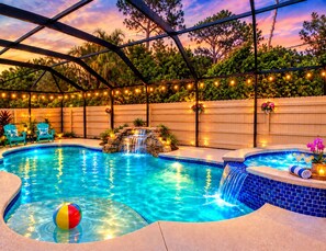 A swimming pool with a waterfall feature, surrounded by a covered area with string lights.