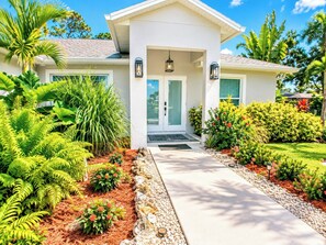 Una casa moderna con porche delantero, cielo despejado y exuberante jardinería tropical.