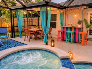 A backyard with a hot tub, wooden table, chairs, and colorful bar stools.