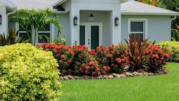 A two-story house with a front porch, a well-maintained lawn, and a variety of colorful flowering plants.