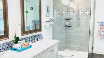 Un baño moderno con cabina de ducha de vidrio, un inodoro blanco y un tocador con espejo y toallero.