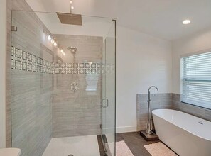 A modern bathroom with a glass-enclosed shower, a freestanding bathtub, and a window with blinds.