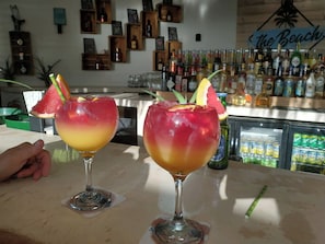 Två drinkar dekorerade med frukt står på bardisken, omgivna av hyllor fulla med spritflaskor.