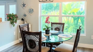 Un comedor con una mesa redonda de cristal, cuatro sillas de madera oscura con asientos acolchados, una lámpara colgante y una ventana con vistas a zonas verdes.