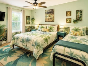A bedroom with a bed, two bedside tables, a ceiling fan, a window with curtains, and wall art.