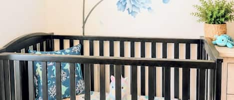 Una cuna con un colchón floral, un aparador de madera y una pared con un mural floral azul.