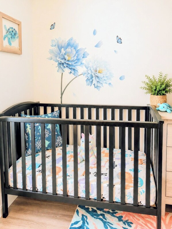 Una cuna con un colchón floral, un aparador de madera y una pared con un mural floral azul.